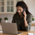 Woman on phone looking at a laptop in her kitchen